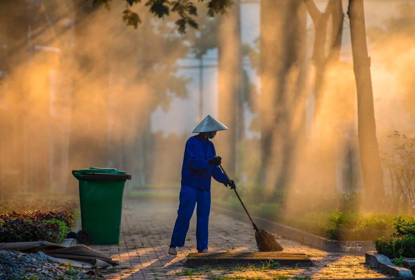Nhân viên vệ sinh quét dọn công viên trong làn sương, góp phần bảo vệ môi trường