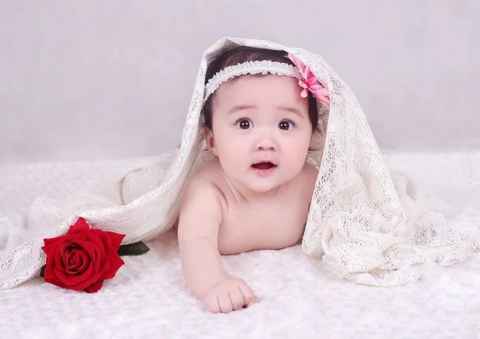 Bé sơ sinh mặc khăn voile và hoa hồng đỏ