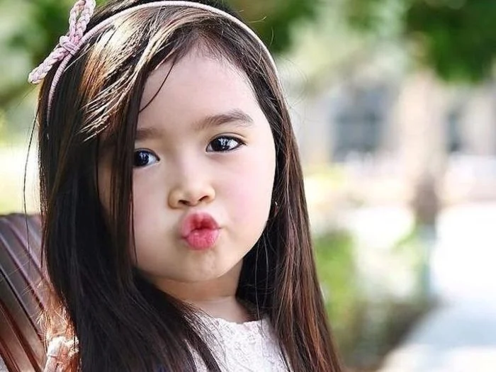 ảnh em bé cute nhếch môi hôn nhìn camera ngoài trời