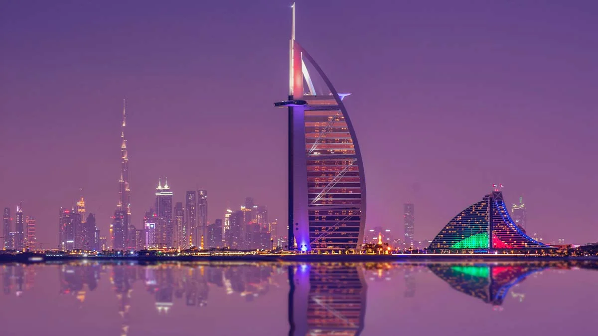 Hình nền máy tính 4K toàn cảnh Dubai về đêm với khách sạn Burj Al Arab, đường chân trời rực rỡ và phản chiếu trên mặt nước
